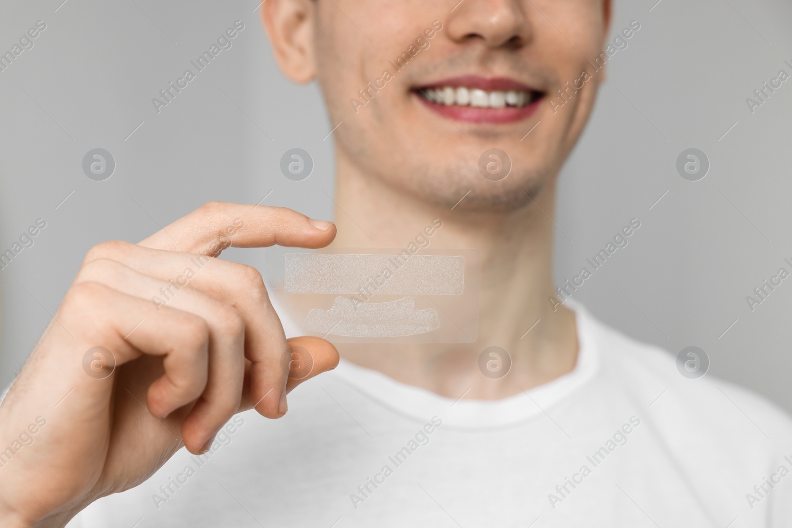 Photo of Young man with whitening strips on grey background, closeup