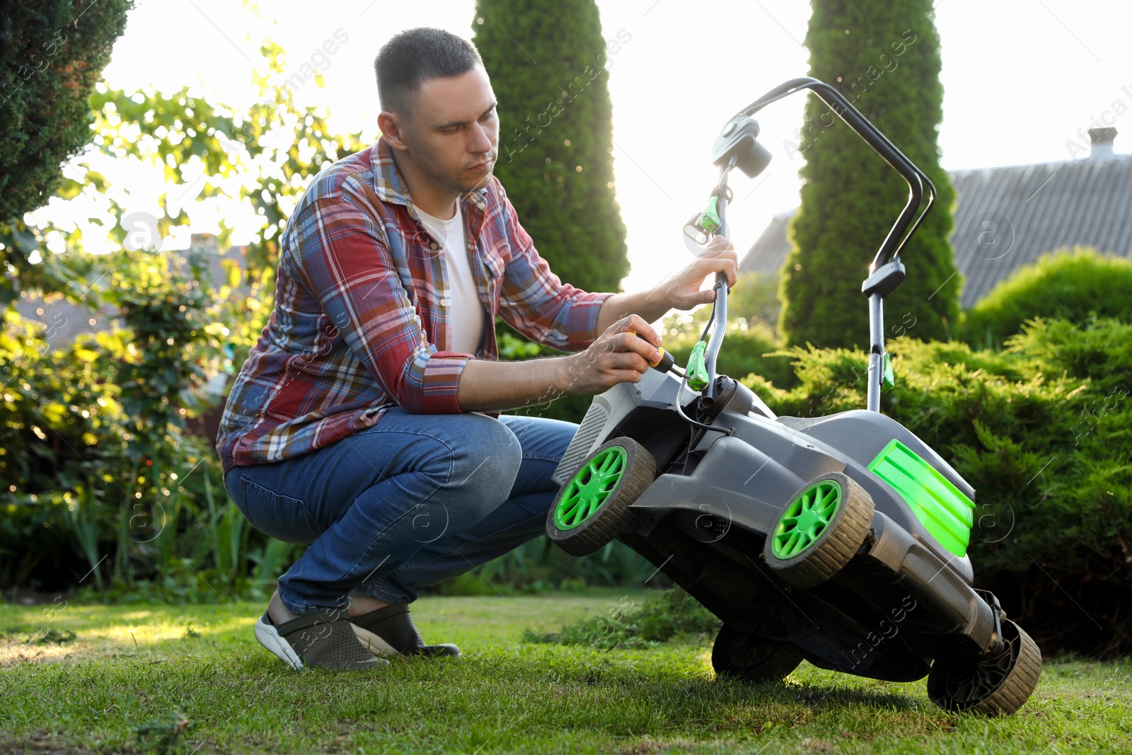 Photo of Man with screwdriver fixing lawn mower in garden