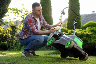 Photo of Man with screwdriver fixing lawn mower in garden