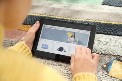 Photo of Woman with credit cards using tablet for online shopping on carpet, closeup