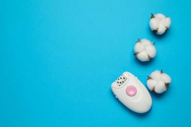 Photo of Modern epilator and fluffy cotton flowers on light blue background, flat lay. Space for text