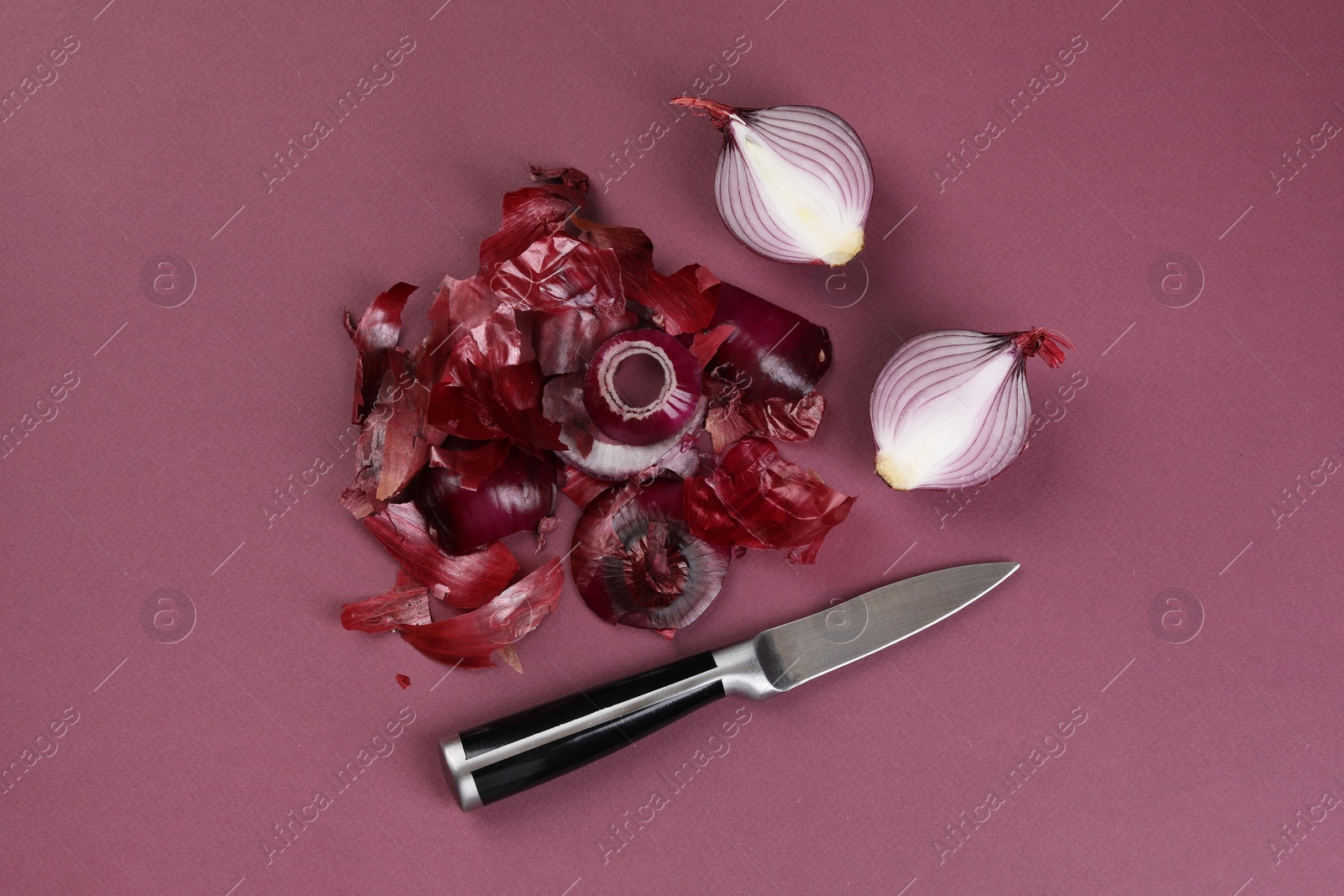 Photo of Cut red onions with peels and knife on dark pink background, flat lay