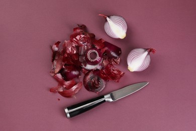 Cut red onions with peels and knife on dark pink background, flat lay