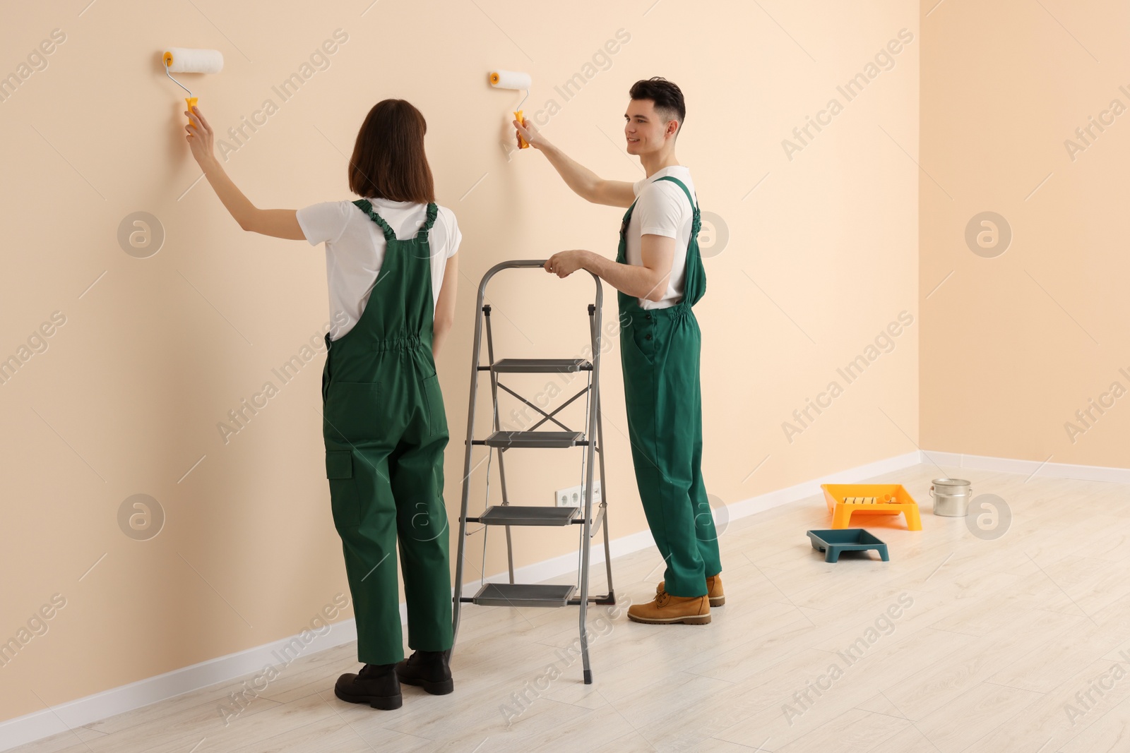 Photo of Young workers painting wall with rollers indoors. Room renovation