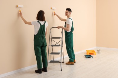 Photo of Young workers painting wall with rollers indoors. Room renovation