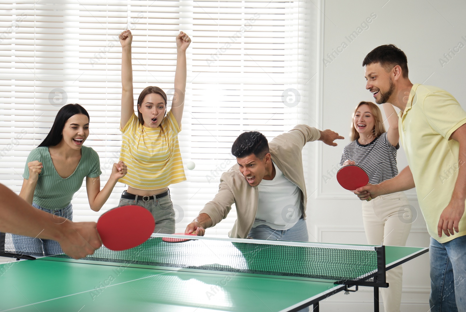 Photo of Happy friends playing ping pong together indoors