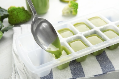 Photo of Putting healthy baby food into ice cube tray, closeup