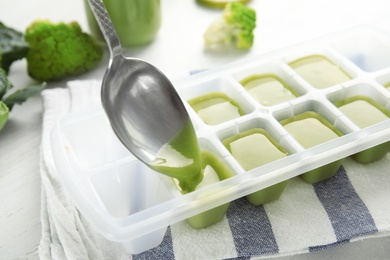 Putting healthy baby food into ice cube tray, closeup