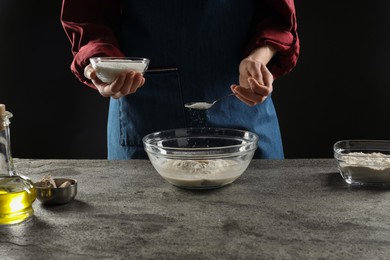 Photo of Making bread. Woman putting sugar into bowl at grey textured table, closeup