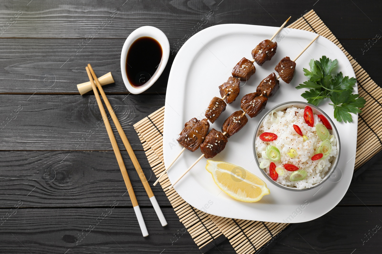 Photo of Tasty chicken meat glazed in soy sauce served with rice on black wooden table, flat lay