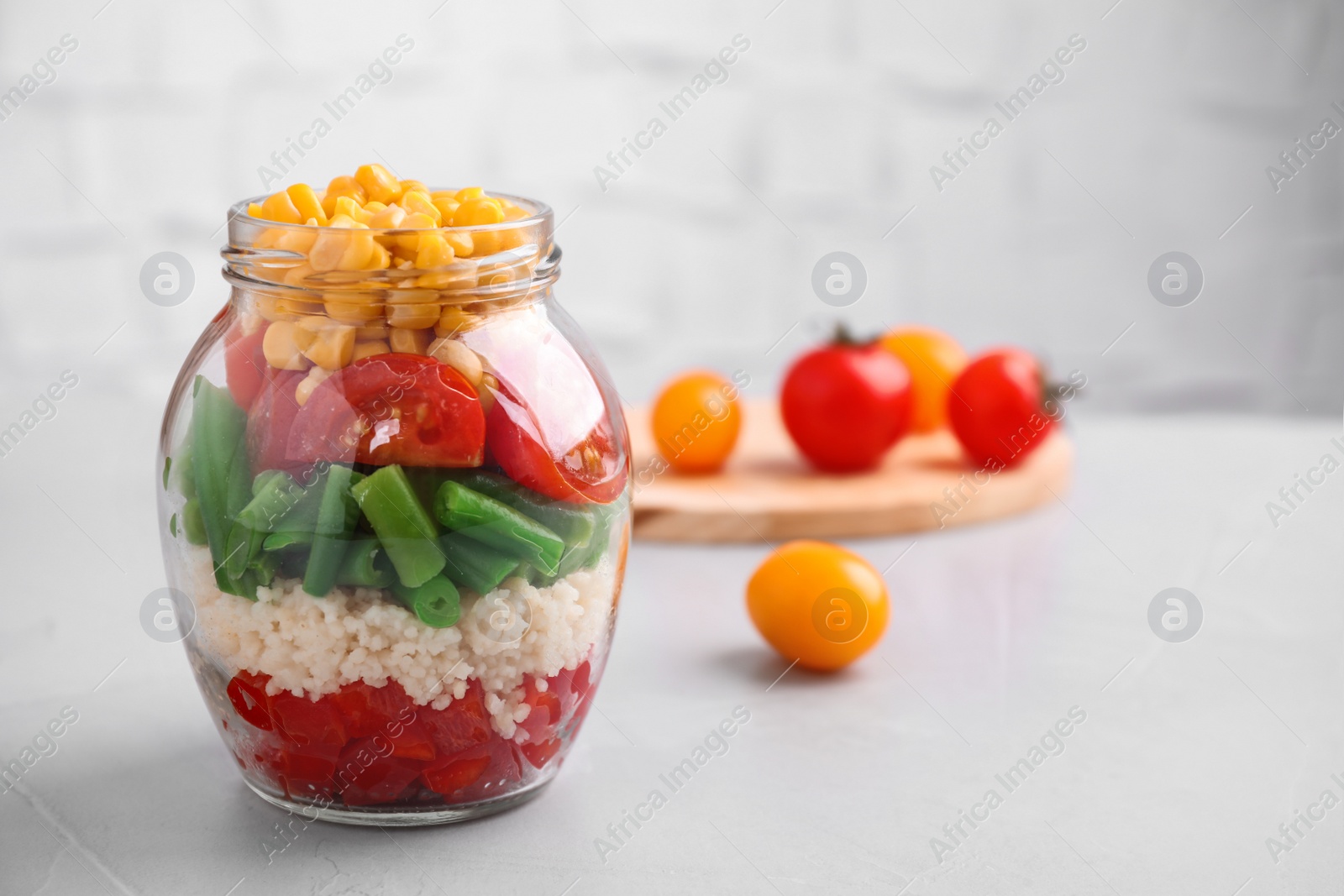 Photo of Healthy salad in glass jar on light table. Space for text