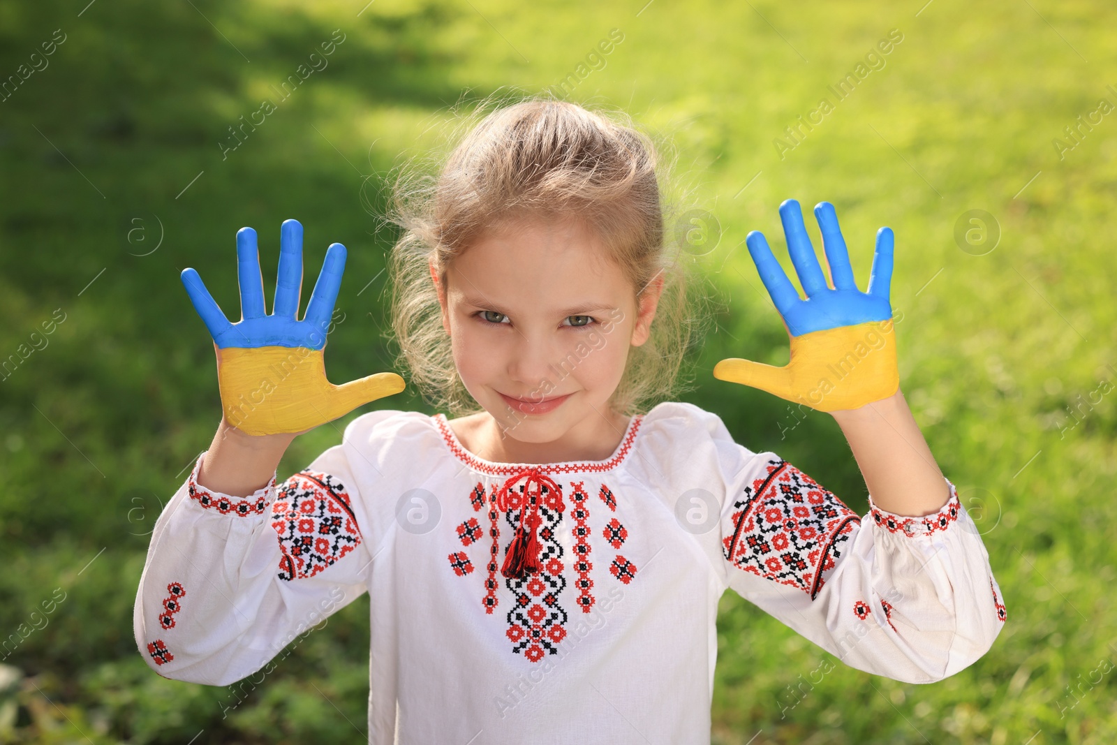 Photo of Little girl with hands painted in Ukrainian flag colors outdoors. Love Ukraine concept