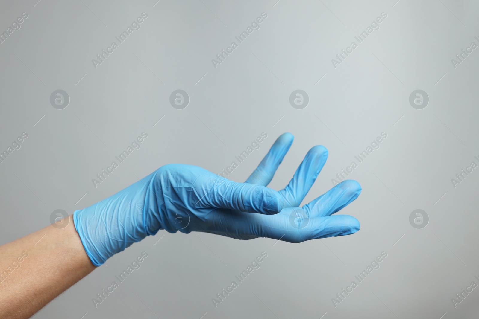 Photo of Doctor wearing light blue medical glove holding something on grey background, closeup