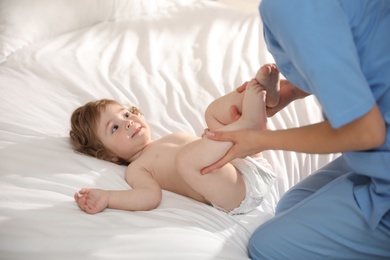 Photo of Orthopedist examining cute little baby on bed