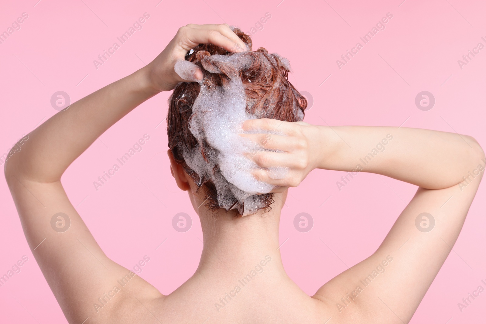 Photo of Young woman washing her hair with shampoo on pink background, back view