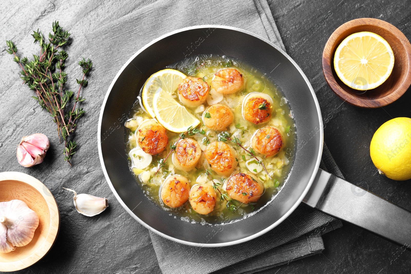 Photo of Delicious scallops with sauce in frying pan and ingredients on dark gray textured table, flat lay