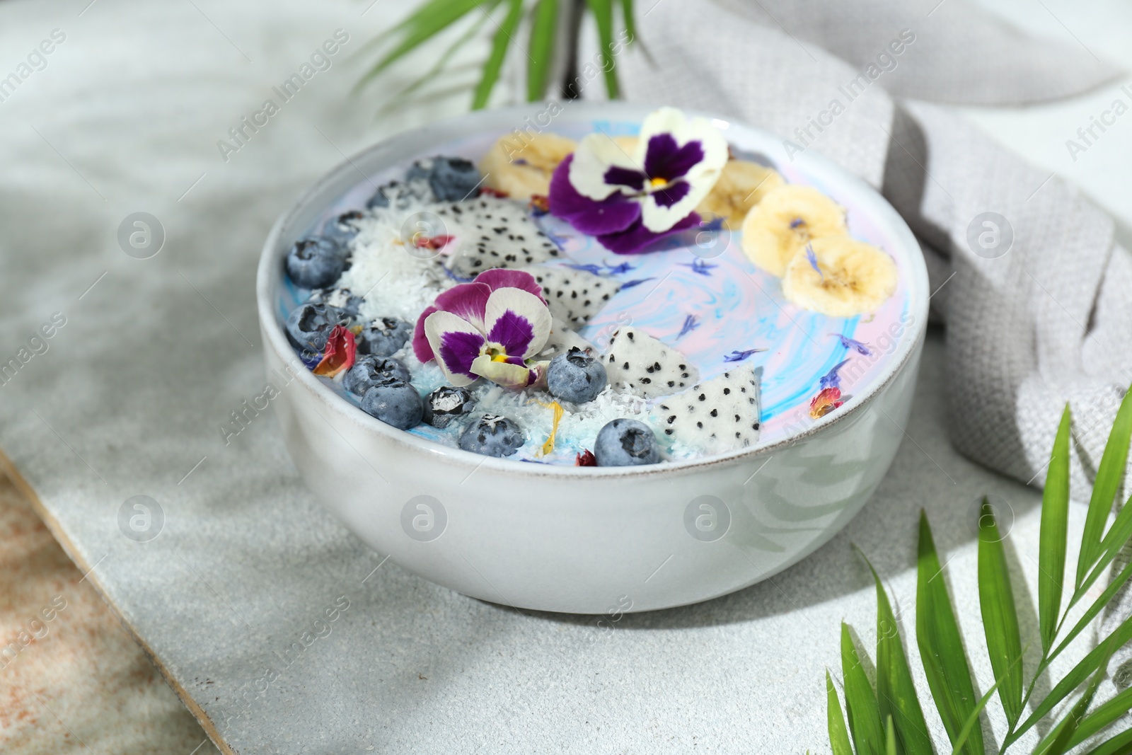 Photo of Delicious smoothie bowl with fresh fruits, blueberries and flowers on color textured table