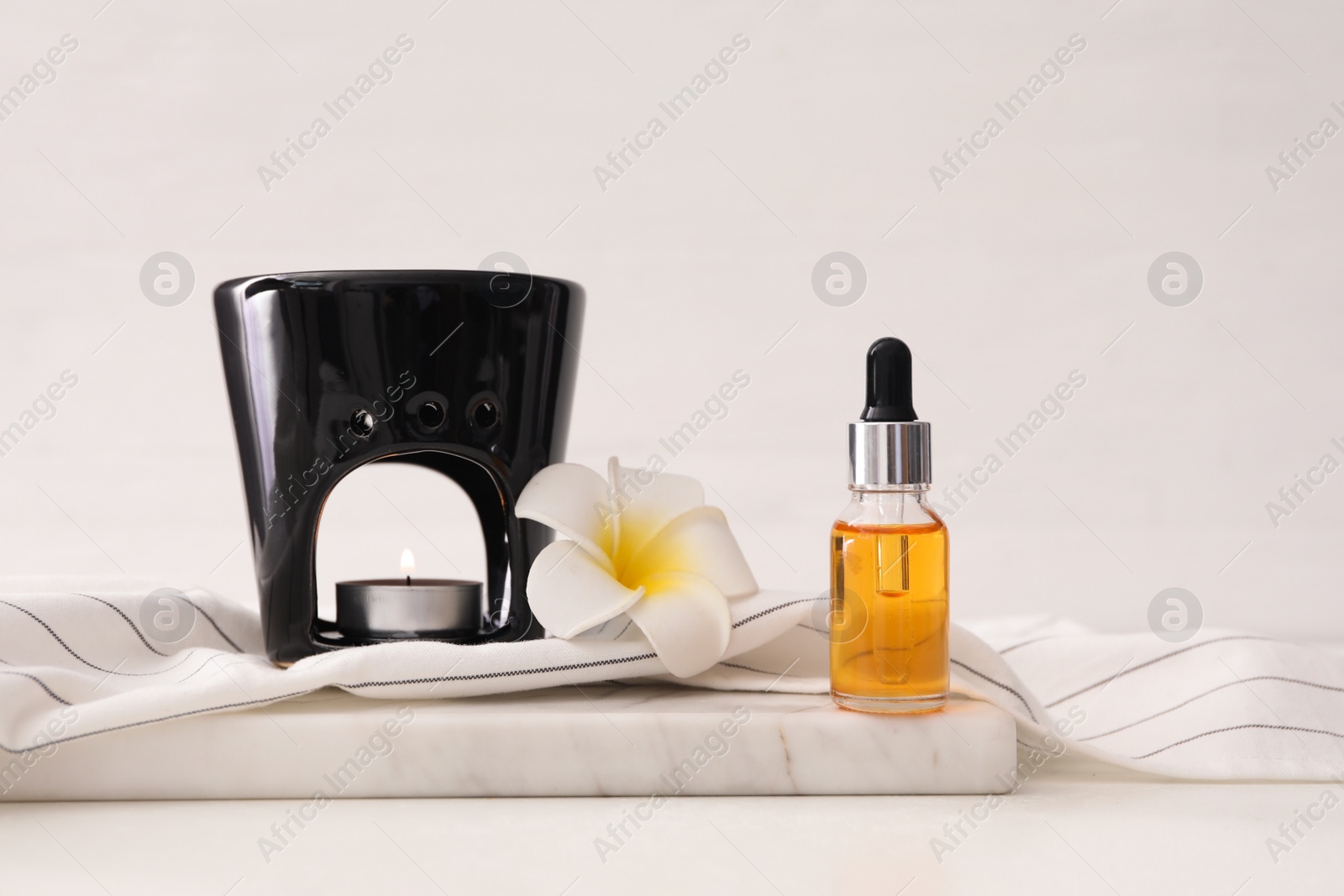 Photo of Aroma lamp, plumeria flower and bottle of essential oil on white table