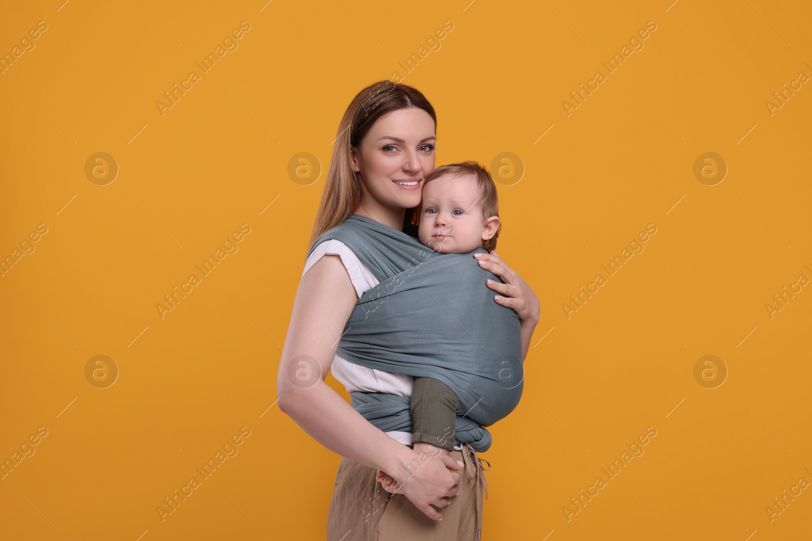 Photo of Mother holding her child in baby wrap on orange background