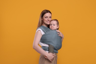 Mother holding her child in baby wrap on orange background