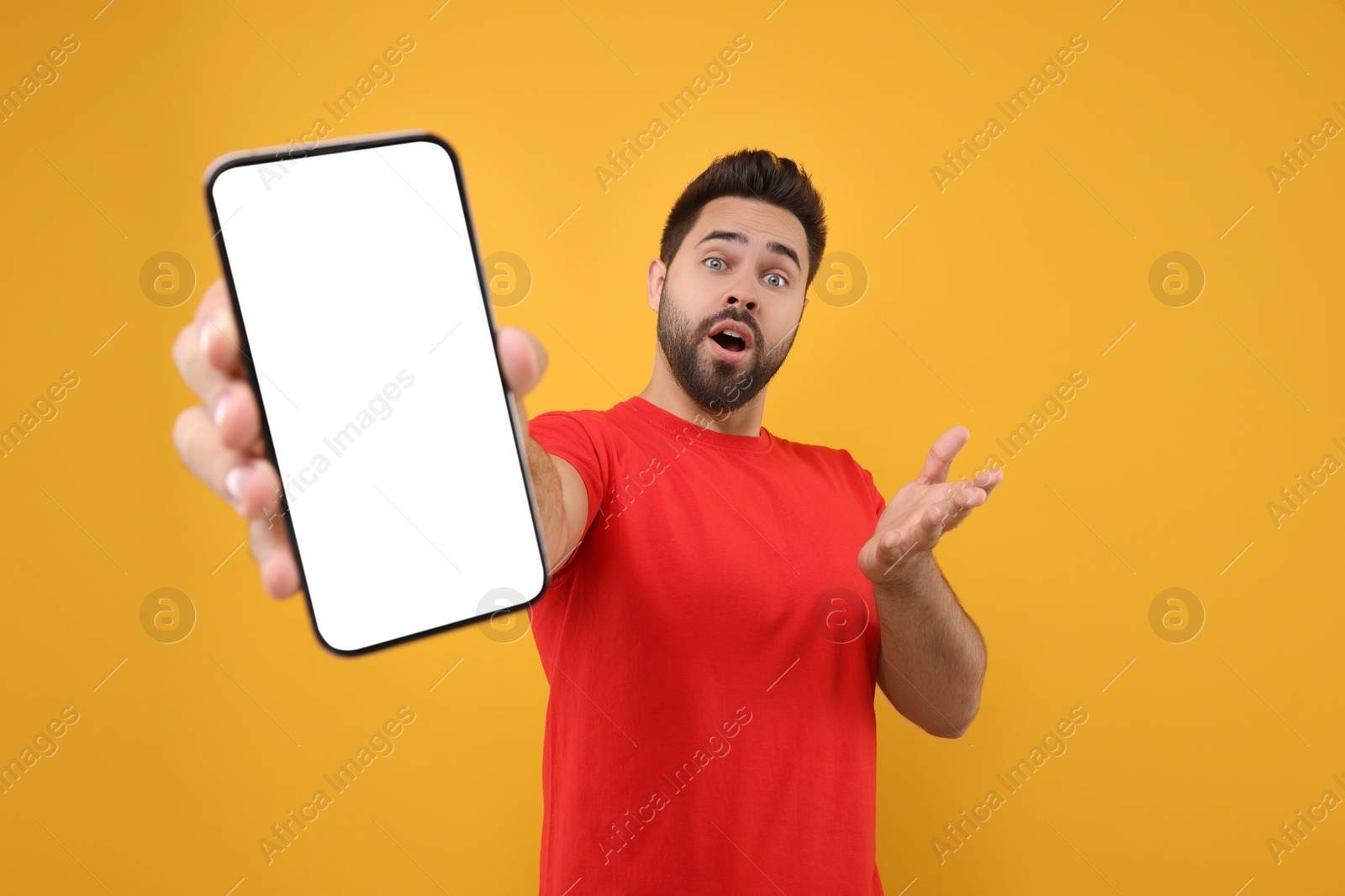 Photo of Surprised man showing smartphone in hand on yellow background