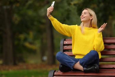 Happy woman having video chat by smartphone in autumn park. Space for text