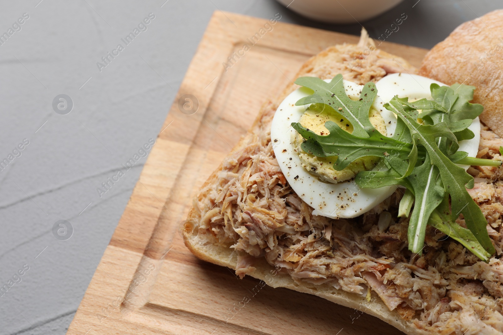 Photo of Delicious sandwich with tuna, boiled egg and greens on light grey table, closeup. Space for text