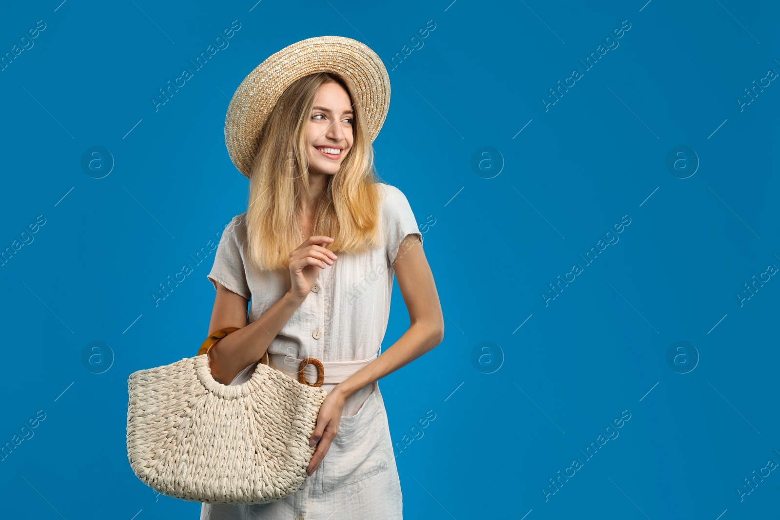 Photo of Beautiful young woman with stylish straw bag on blue background. Space for text