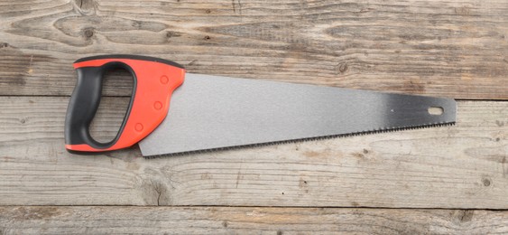 Photo of Saw with colorful handle on wooden background, top view