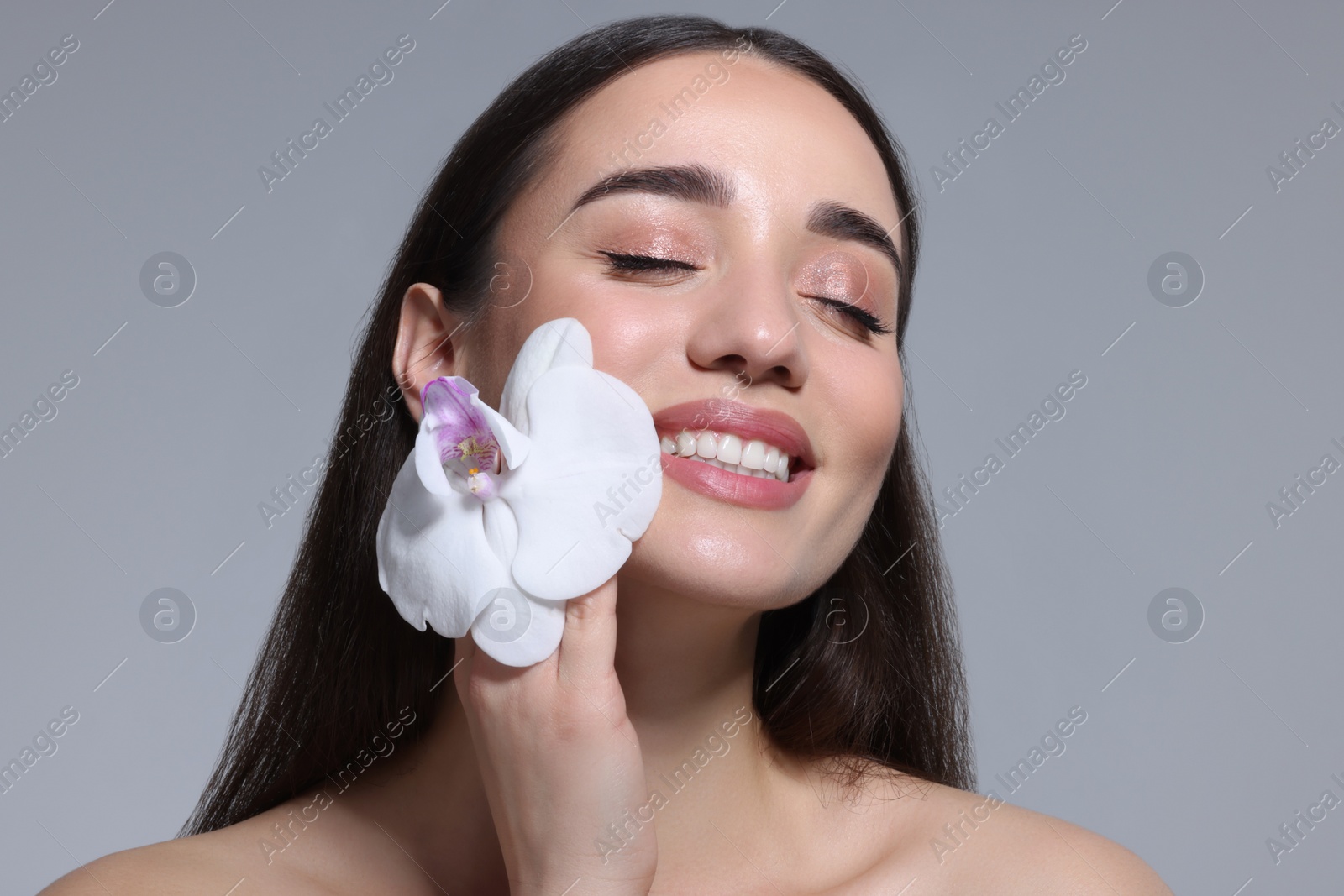 Photo of Portrait of smiling woman with orchid flower on grey background