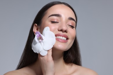 Portrait of smiling woman with orchid flower on grey background