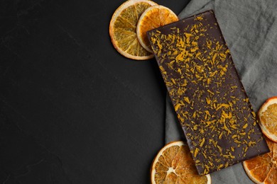 Photo of Chocolate bar with freeze dried orange on black table, flat lay. Space for text