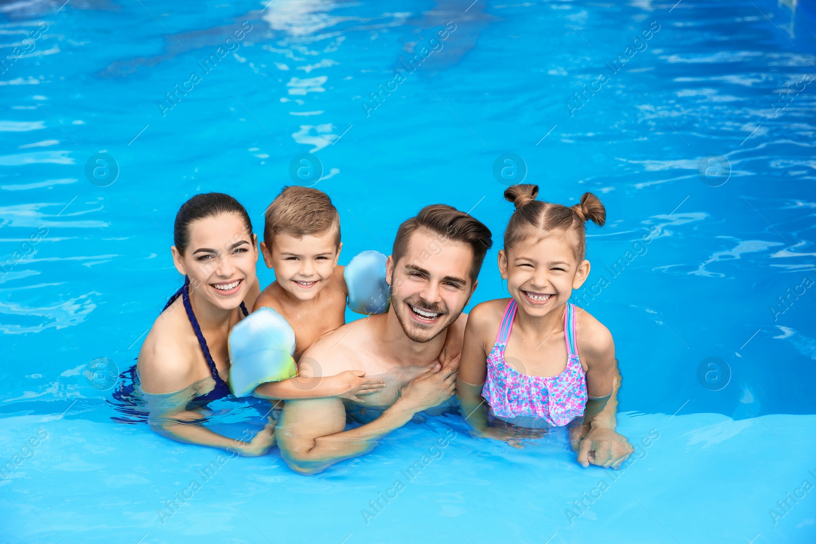 Photo of Young family with little children in swimming pool on sunny day