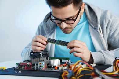 Male technician repairing motherboard at table against light background