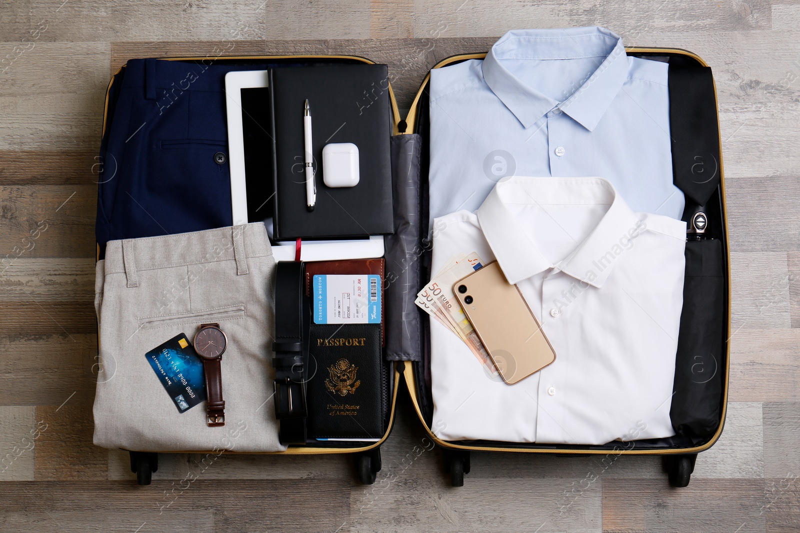 Photo of Packed suitcase with business trip stuff on wooden surface, flat lay