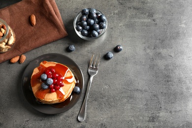 Stack of tasty pancakes with berries and syrup on table, top view