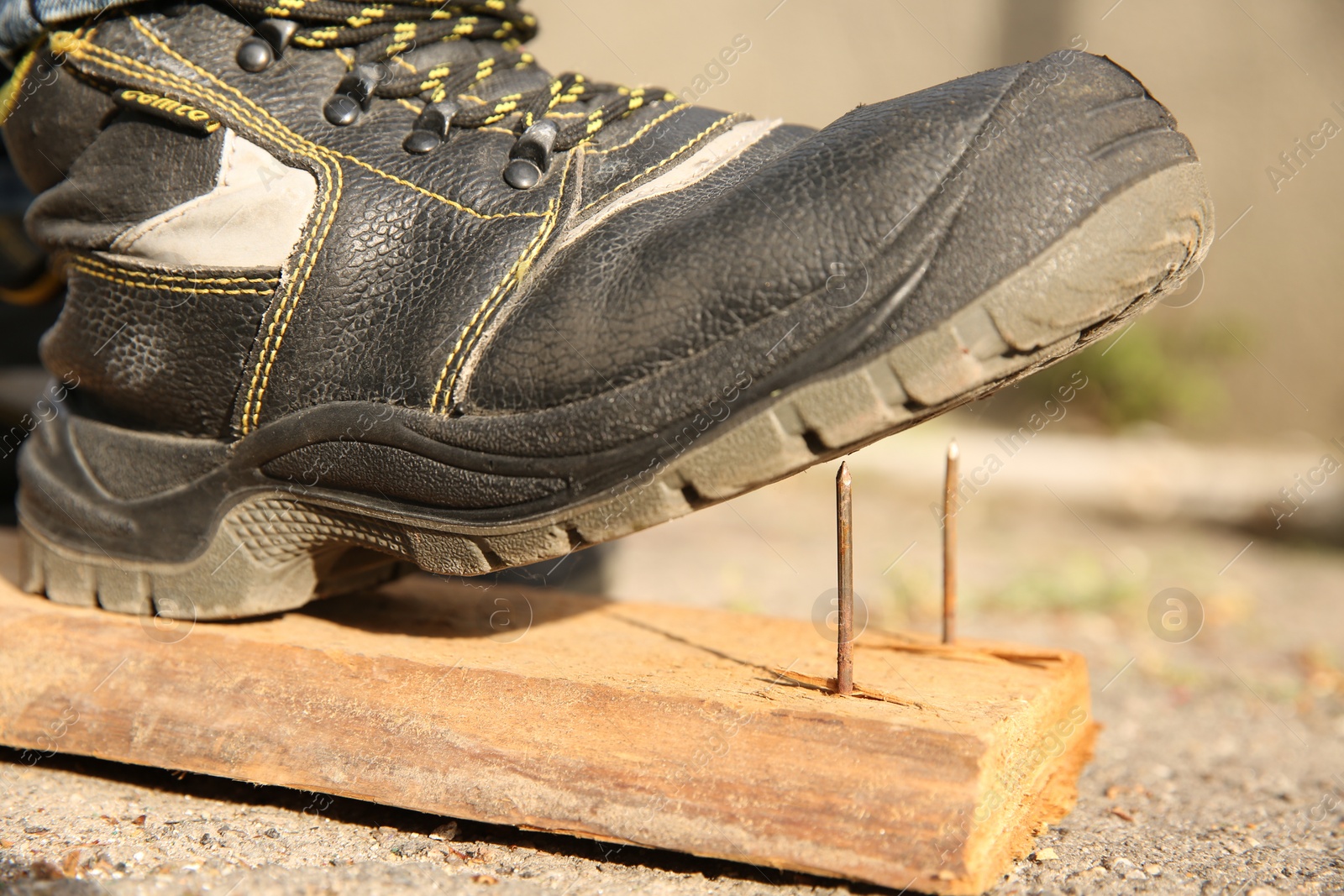 Photo of Careless worker stepping on nails in wooden plank outdoors, closeup