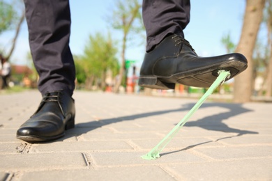 Photo of Man stepping in chewing gum on sidewalk. Concept of stickiness