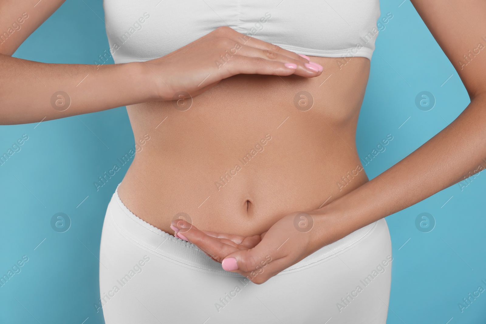 Photo of Woman in underwear holding something near her belly on light blue background, closeup. Healthy stomach