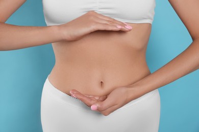 Woman in underwear holding something near her belly on light blue background, closeup. Healthy stomach