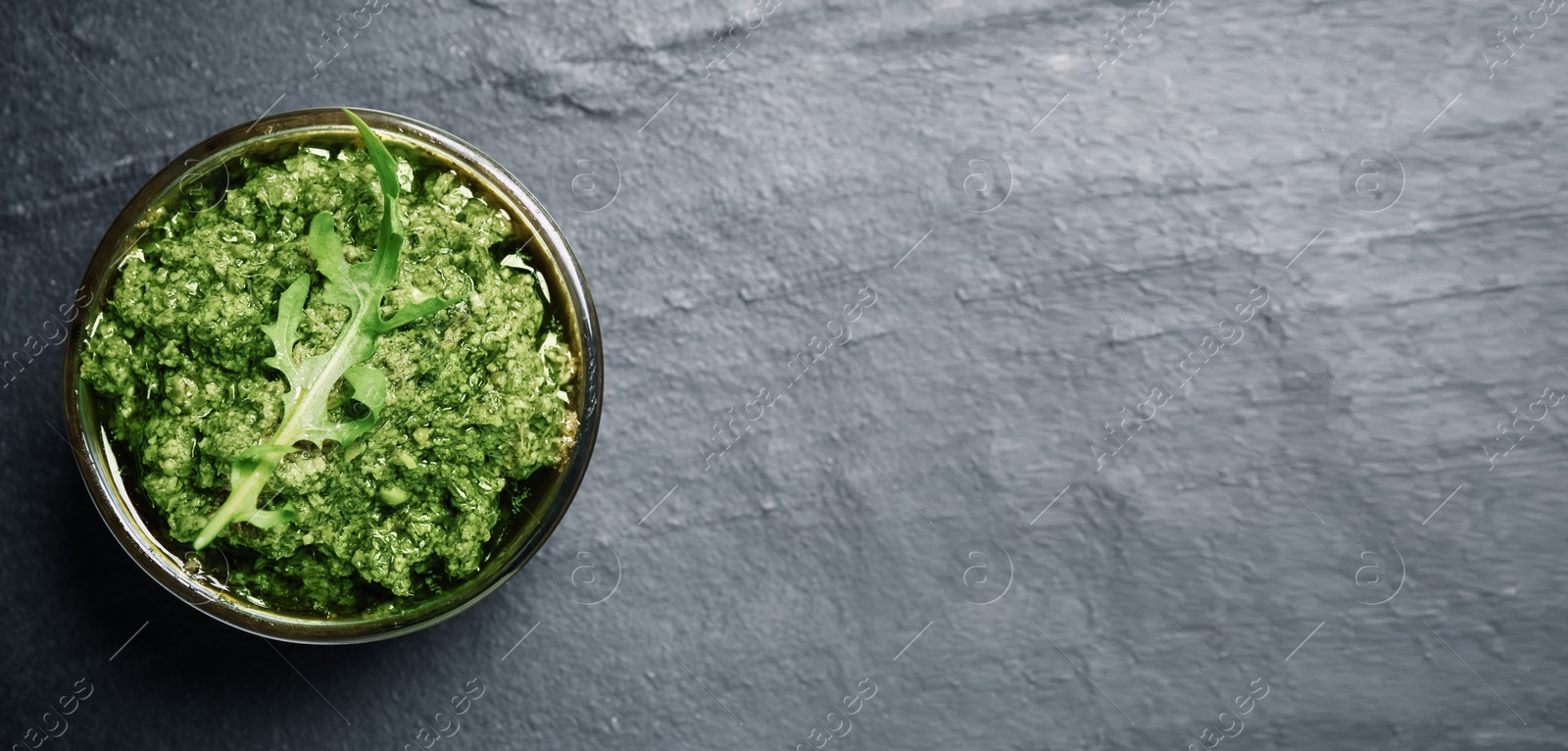 Image of Top view of bowl with arugula pesto on grey table, space for text. Banner design 