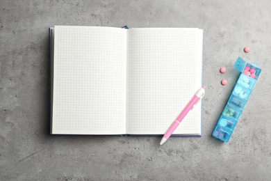 Photo of Copybook with space for text, pen and pills in container on gray background, flat lay. Medical care