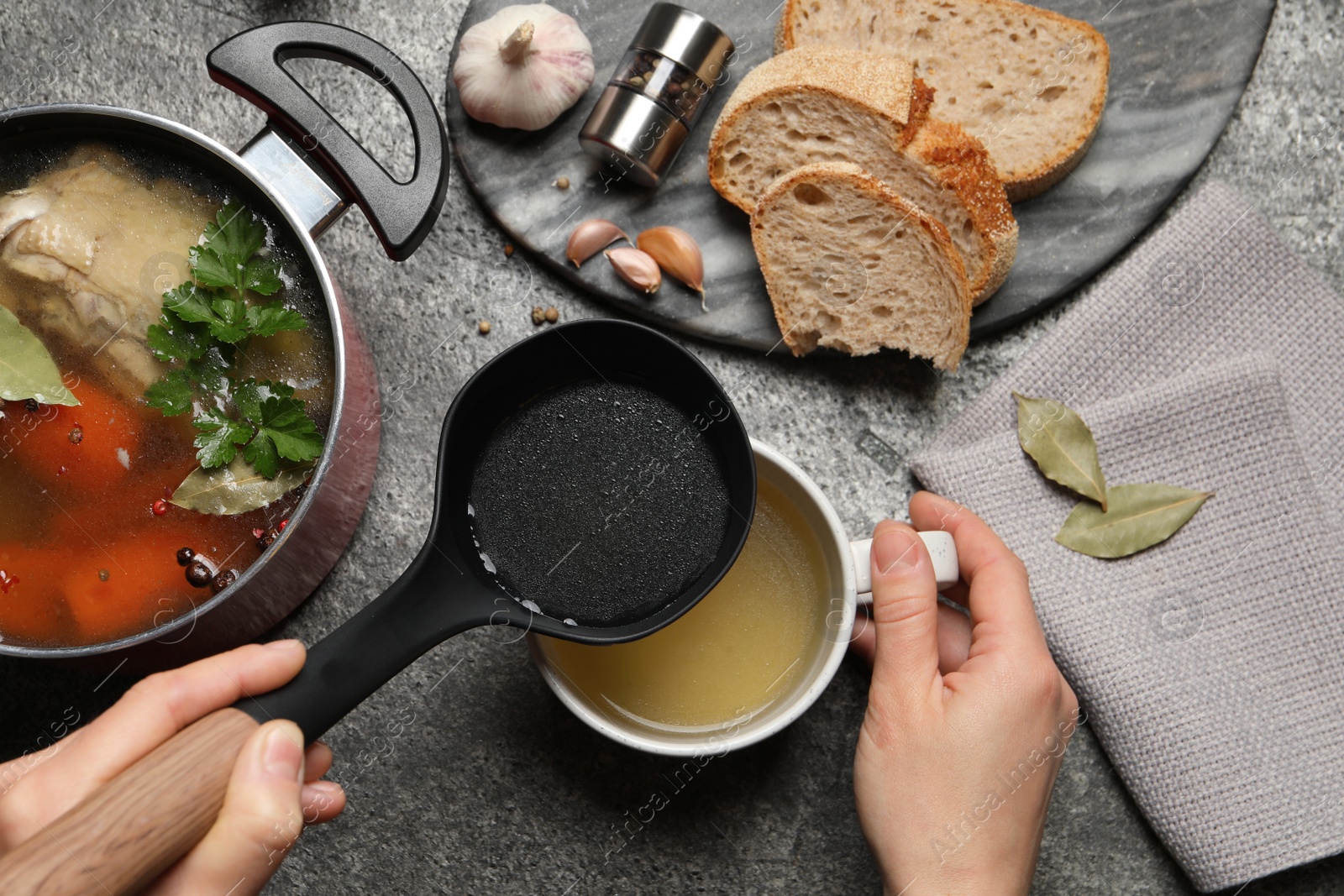 Photo of Woman pouring hot delicious bouillon into cup at grey table, top view