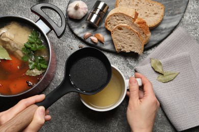 Woman pouring hot delicious bouillon into cup at grey table, top view