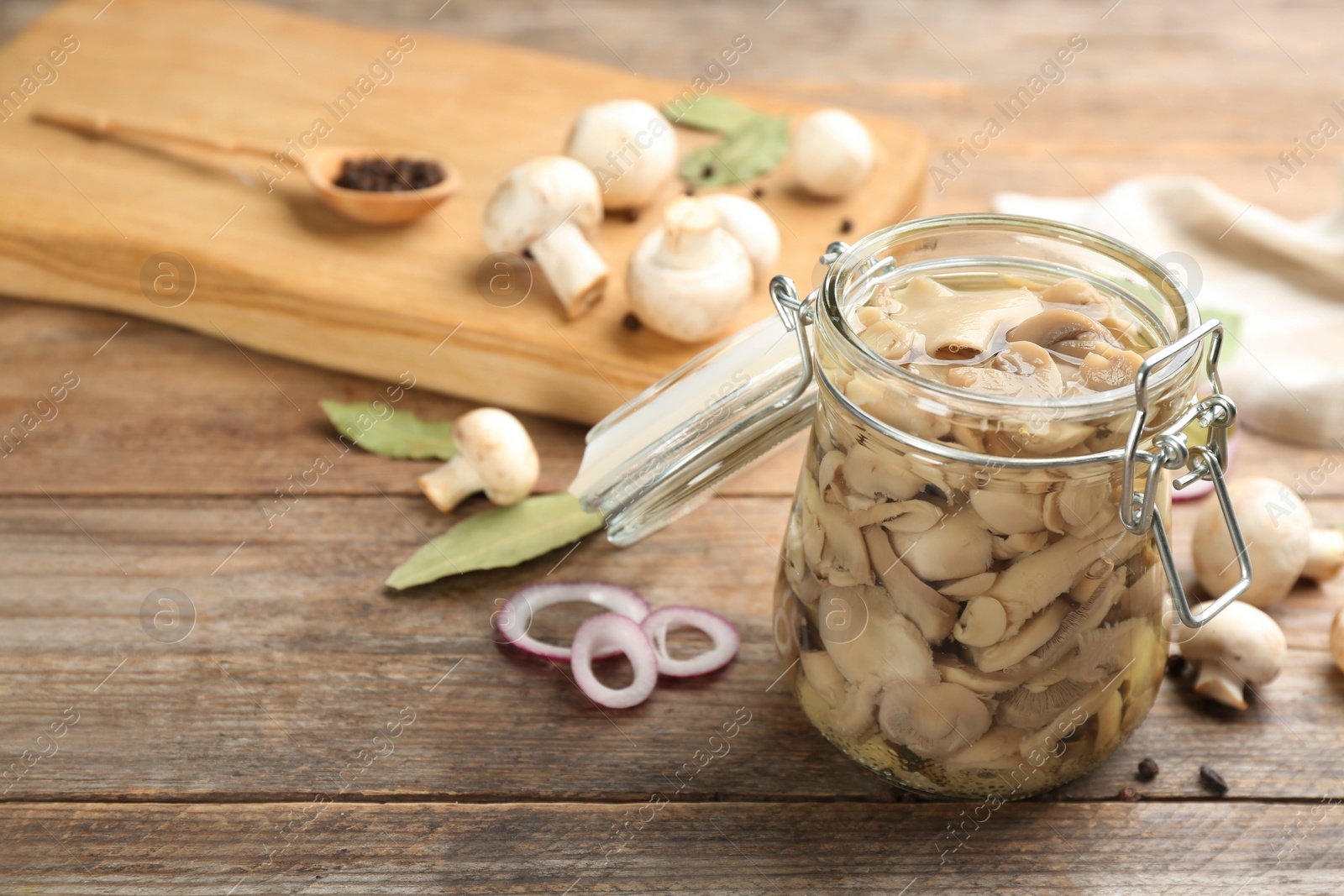 Photo of Glass jar of pickled mushrooms on wooden table. Space for text