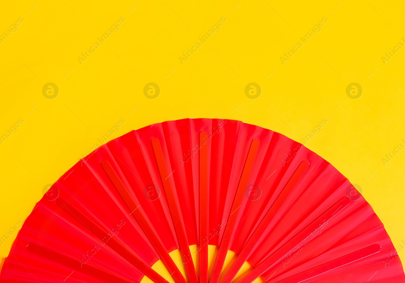 Photo of Red hand fan on yellow background, top view