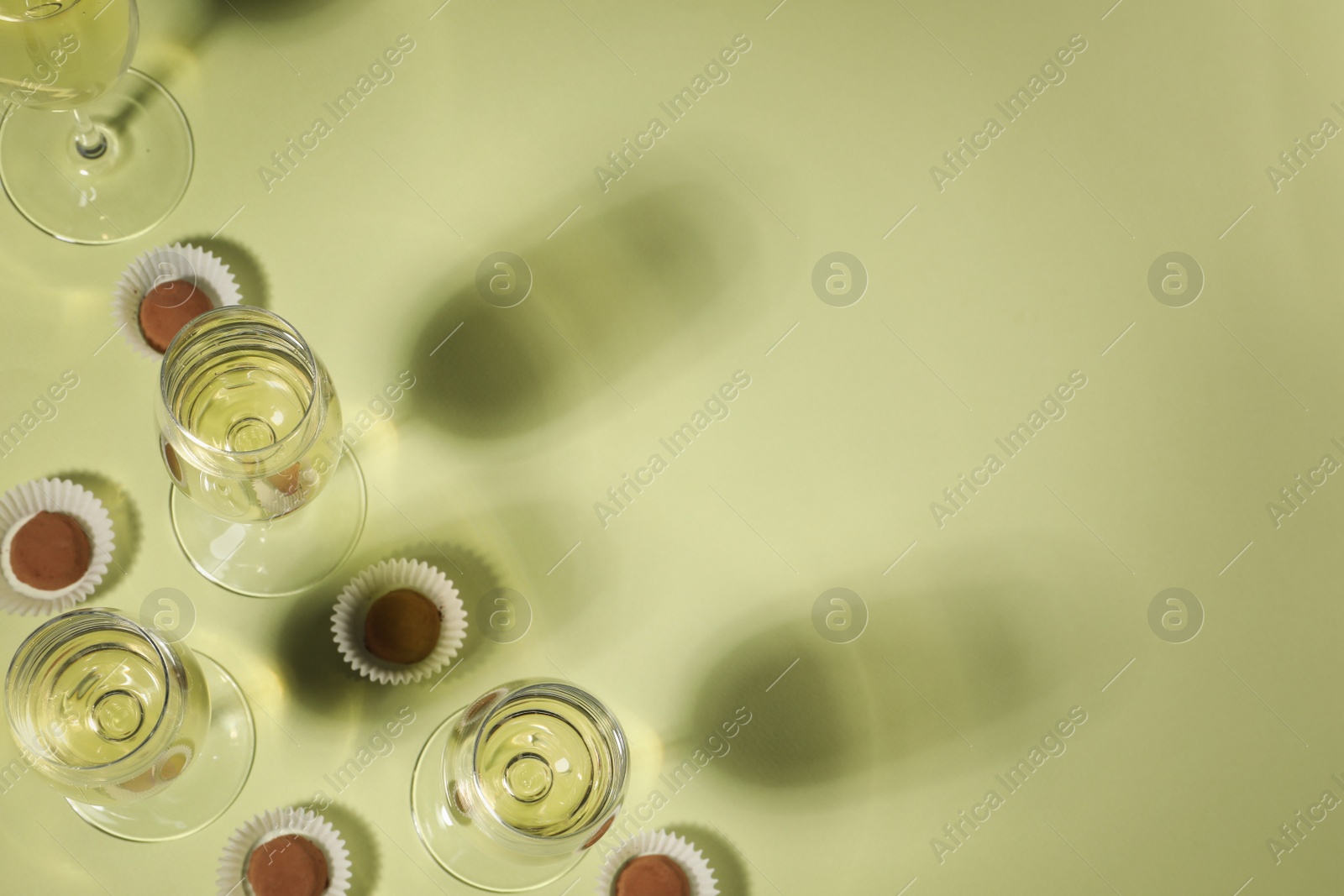 Photo of Glasses of delicious sparkling wine and chocolate truffles on light yellow background, above view. Space for text