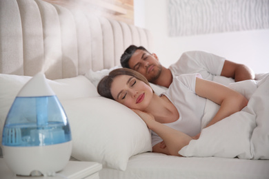 Couple sleeping in bedroom with modern air humidifier