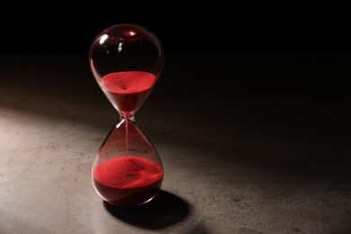 Photo of Hourglass with red flowing sand on grey table. Space for text