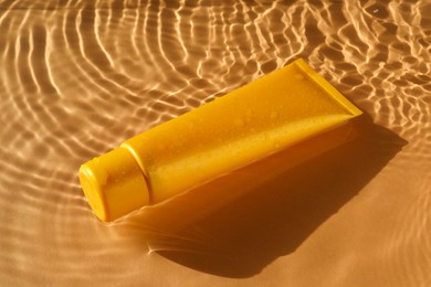 Photo of Tube with moisturizing cream in water on orange background